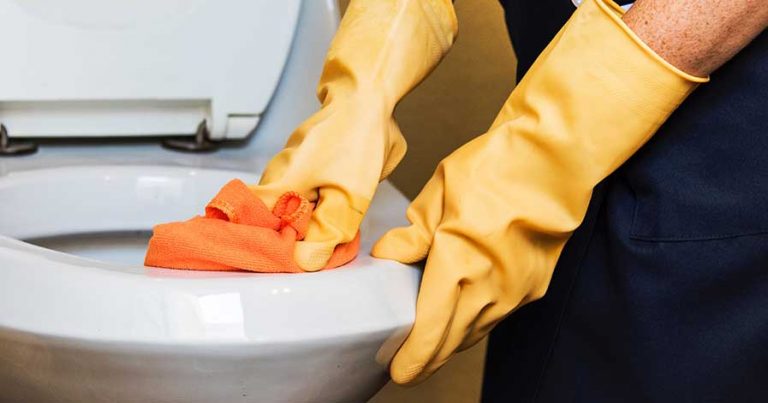 Someone cleaning a toilet while wearing rubber gloves