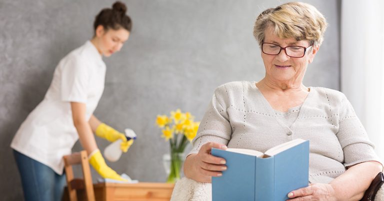 a senior citizen reading a book while a cleaning service works