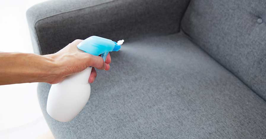 Spraying cleaner on a couch to eliminate odors