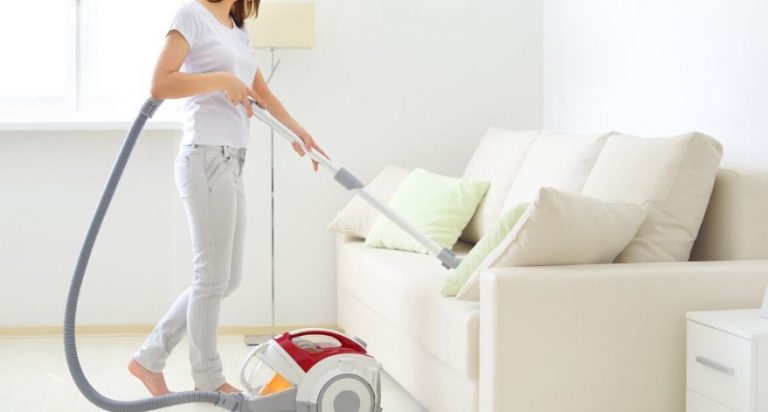A woman is vacuuming her couch.