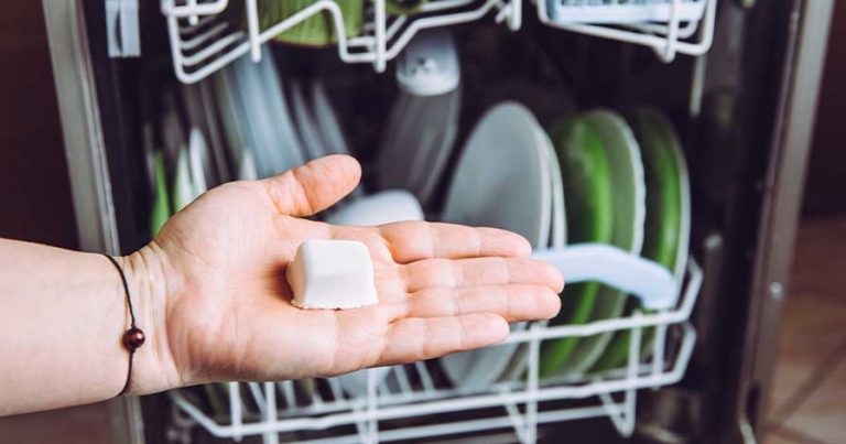 A person holding a dishwasher pod in front of an open dishwasher.