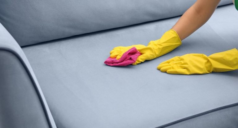 Two hands wearing rubber gloves scrubbing a cough with a red sponge